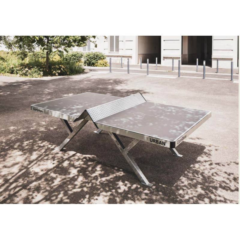 Table ping pong pliable extérieur métallique en plein air, avec structure en X et filet central, près d’un bâtiment.